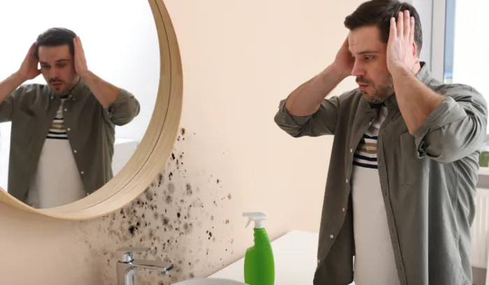 uomo osserva il muro di casa macchiato dalla muffa, causata a sua volta dall'umidità, e si mette le mani sui capelli