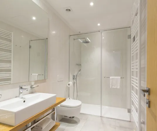 bagno moderno dai toni chiari e finiture in legno, con box doccia in vetro e piatto doccia in pietra bianca