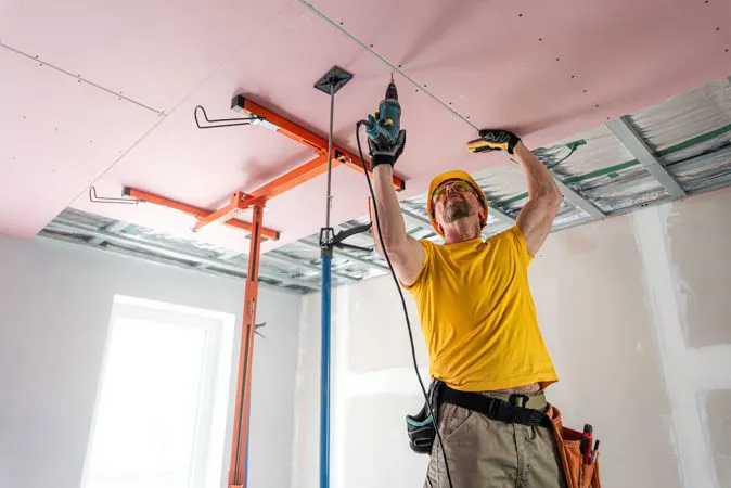 Operaio mentre avvita delle lastre in cartongesso al soffitto per le costruzioni a secco